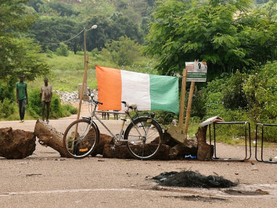 Le drapeau ivoirien et des troncs d'arbres pour bloquer une route d'accès à Daoukro, le 2 novembre 2020 - SIA KAMBOU [AFP]