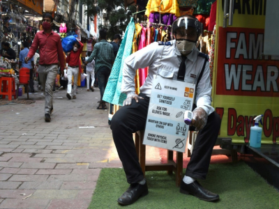 Un gardien tient une pancarte informant sur les mesures de prévention contre le coronavirus, devant une boutique d'un marché bondé avant la grande fête hindoue de Diwali, à New Delhi le 12 novembre 2020 - Money SHARMA [AFP]
