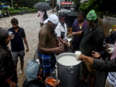Des bénévoles distribuent du riz au lait à des habitants au bord d'une route inondée après le passage du cyclone Nivar, à Pondichéry en Inde le 26 novembre 2020 - Arun SANKAR [AFP]