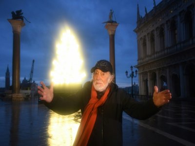 L'artiste italien Fabrizio Plessi pose devant son installation lumineuse évoquant un sapin de Noël sur la place Saint-Marc à Venise le 4 décembre 2020 - ANDREA PATTARO [AFP]