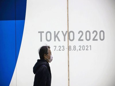 Un piéton passe devant un mur donnant les dates des prochains Jeux Olympiques, décalés à l'été prochain, le 22 janvier 2021 à Tokyo - Behrouz MEHRI [AFP]