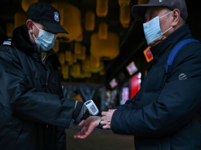 Un agent contrôle la température d'un client à l'entrée d'un centre commercial, le 22 janvier 2021 à Wuhan, en Chine - Hector RETAMAL [AFP]