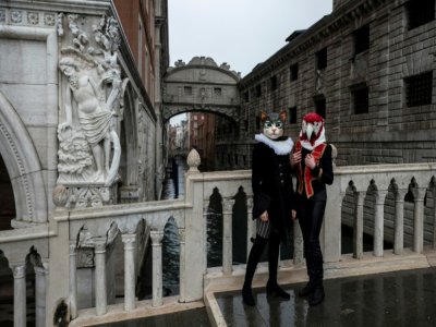 Des artisans vénitiens portant des masques et costumes de carnaval posent près du pont des Soupirs, le 7 février 2021 à Venise (Italie) - Marco Bertorello [AFP]