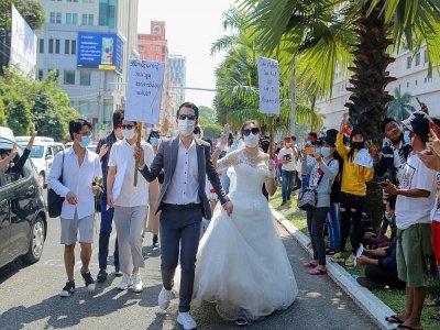 Des manifestants en tenue de noces défilent à Rangoun avec une pancarte (D) affirmant "notre mariage peut attendre, mais pas ce mouvement", le 9 février 2021 - STR [AFP]
