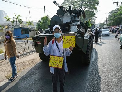 Un manifestant brandit des pancartes pro-démocratie près de véhicules blindés de l'armée à Rangoun, le 15 février 2021 - YE AUNG THU [AFP]
