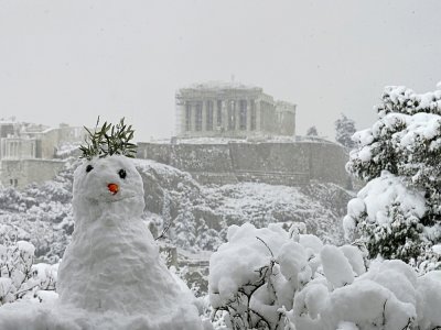 Un bonhomme de neige devant une vue du Parthénon sur l'Acropole recouverte de neige à Athènes le 16 février 2021 - ARIS MESSINIS [AFP]