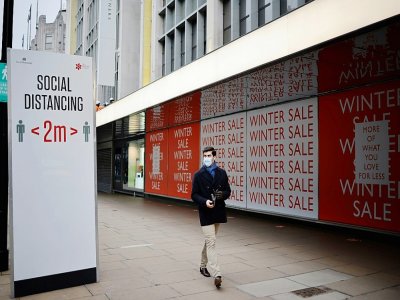 Un passant près d'un panneau incitant au respect de la distanciation sociale, le 8 janvier 2021 à Londres - Tolga Akmen [AFP/Archives]