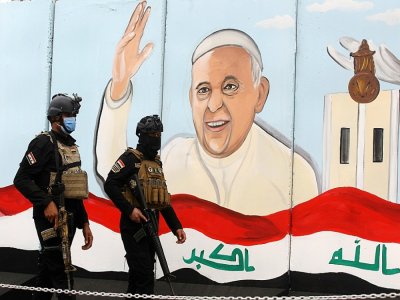 Des forces de sécurité irakiennes devant une  fresque murale représentant le pape François, le 4 mars 2021 à Bagdad - AHMAD AL-RUBAYE [AFP]