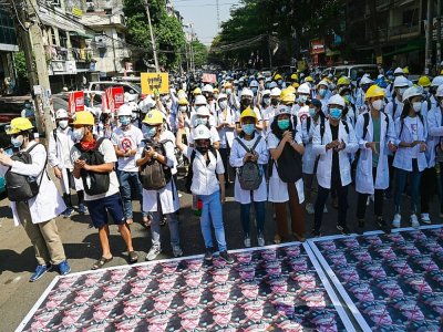 Du personnel médical et des étudiants manifestent contre le coup d'Etat à Rangoun, le 5 mars 2021, devant des photos du chef de la junte, le général Min Aung Hlaing, collées à même le bitume, dans le but de freiner la progression des soldats, réticen - STR [AFP]