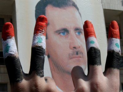 Deux hommes avec les doigts peints dans les couleurs du drapeau syrien font le V de la victoire devant une affiche du président Bachar a-Assad dans le  centre de Damas, le 29 mars 2011 - ANWAR AMRO [AFP/Archives]