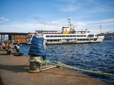 Un ferry est amarré au port de Karakoy à Istanbul alors que des gens sont assis sur la rive du Bosphore, le 8 février 2021 à Istanbul. - Ozan KOSE [AFP]