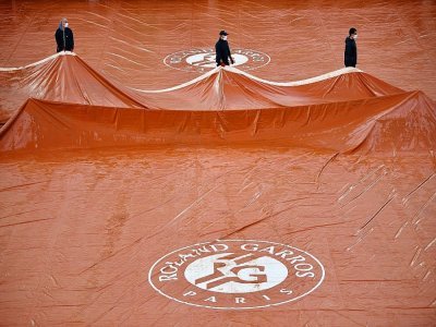 Des travailleurs retirent des bâches sur la surface du court Suzanne Lenglen après la pluie, lors de la huitième journée du tournoi de tennis Roland Garros, le 4 octobre 2020 à Paris - Anne-Christine POUJOULAT [AFP/Archives]
