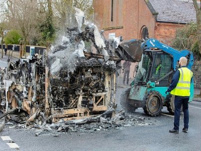 Des employés du conseil municipal de Belfast  nettoient les restes d'un bus brûlé à  Shankill Road le 8 avril 2021 - PAUL FAITH [AFP]