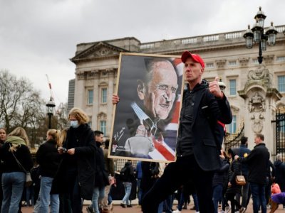Un homme pose avec le portrait du prince Philip devant le Palais de Buckingham, au lendemain de son décès, le 10 avril 2021 à Londres - Tolga Akmen [AFP]