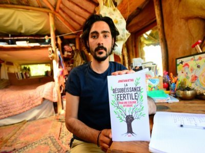 Jonathan Attias montre son livre "La désobéissance fertile", assis dans sa cabane, au milieu des bois de Chasteaux, en Corrèze, le 23 avril 2021 - MEHDI FEDOUACH [AFP]