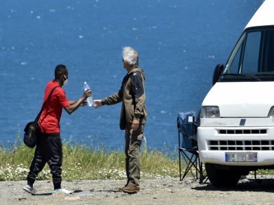 Un voyageur en camping-car donne une bouteille d'eau à un jeune migrant le 12 mai 2021 sur une route menant à Cerbère (Pyrénées-orientales - RAYMOND ROIG [AFP]