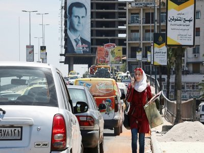 Une passante au téléphone avec en arrière-plan un portrait de Bachar al-Assad, dans une rue de Damas le 25 mai 2021. - LOUAI BESHARA [AFP]
