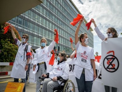 Des professionnels de santé du mouvement Extinction Rebellion agitent des rubans rouges lors d'une manifestation devant les locaux de l'OMS à Genève, le 29 mai 2021 - Fabrice COFFRINI [AFP]