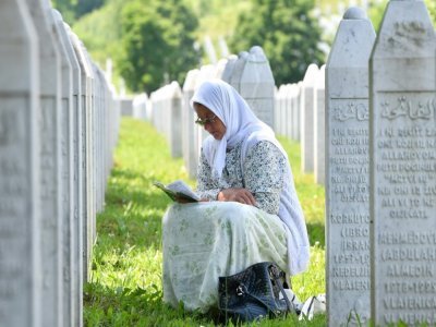 Une musulmane bosniaque lit un livre de prières au milieu des pierres tombales de proches tués lors du massacre de Srebrenica (Bosnie-Herzégovine) en 1995, au cimetière du Mémorial de Srebrenica à Potocari, le 8 juin 2021 - ELVIS BARUKCIC [AFP]