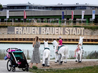 Des enfants jouent face à une pancarte avec le slogan "Les femmes construisent la ville" à Seestadt, dans la banlieue de Vienne, le 8 juin 2021 - JOE KLAMAR [AFP]