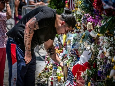 Un homme dépose des fleurs sur le mur du souvenir improvisé en hommage aux victimes de l'effondrement de  l'immeuble à Surfside, le 4 juillet 2021 - Giorgio VIERA [AFP]