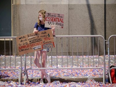 Une spectatrice tient deux pancartes pour remercier les "travailleurs essentiels" de la pandémie de coronavirus, honorés lors d'une parade à New-York le 7 juillet 2021 - Ed JONES [AFP]