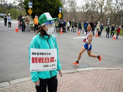 Une volontaire de l'organisation japonaise invite, via sa pancarte, le public à se tenir loin du parcours du semi-marathon de Sapporo, le 5 mai 2021 - Charly TRIBALLEAU [AFP/Archives]