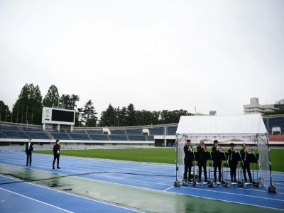 Cinq trompettistes ont joué une mélodie entraînante, sous un kiosque qui les abritait de la bruine, pendant la cérémonie d'arrivée de la flamme olympique à Tokyo organisée dans un stade vide le 9 juillet 2021 - CHARLY TRIBALLEAU [AFP]