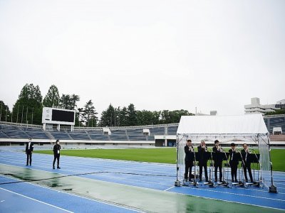 Cinq trompettistes ont joué une mélodie entraînante, sous un kiosque qui les abritait de la bruine, pendant la cérémonie d'arrivée de la flamme olympique à Tokyo organisée dans un stade vide le 9 juillet 2021 - CHARLY TRIBALLEAU [AFP]