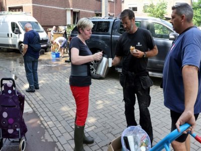 Une habitante sert du café à des voisins nettoyant leurs maisons endommagées par les inondations à Angleur, près de Liège, le 17 juillet 2021 - François WALSCHAERTS [AFP]