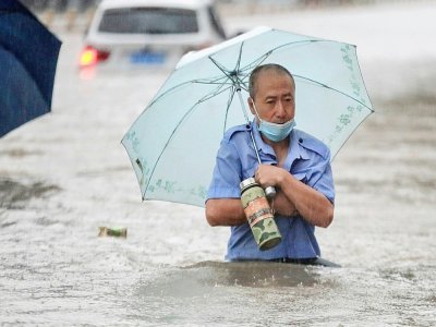 Un homme avance dans une rue inondée de Zhengzhou, placée en alerte rouge après des orages violents qui se sont abattus sur cette métropole du centre de la Chine, le 20 juillet 2021 - STR [AFP]
