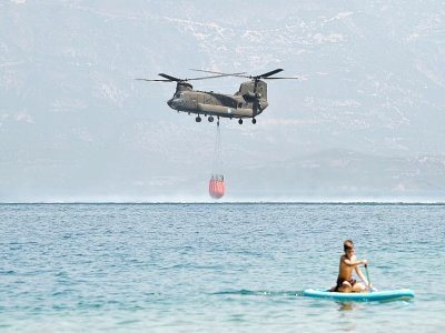 Un vacancier pratiquant le stand up paddle (planche à rame) observe un hélicoptère se ravitailler en eau près de la plage de Lambiri à Patras (Grèce) le 1er août 2021 - Louisa GOULIAMAKI [AFP]