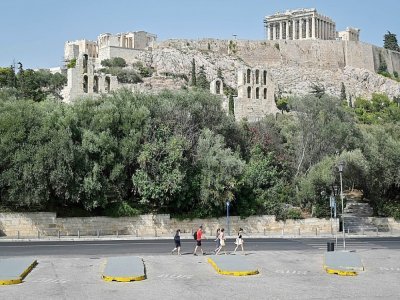 De rares touristes passent au pied de l'Acropole à Athènes, fermée aux heures les plus chaudes de la journée en raison de la "pire canicule" en trente ans en Grèce, le 2 août 2021 - LOUISA GOULIAMAKI [AFP]