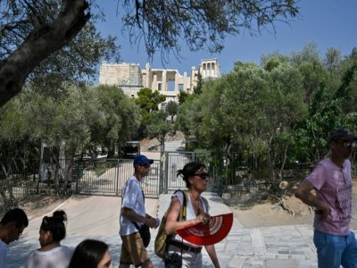 Des touristes restent à l'ombre, devant les portes closes du site archéologique de l'Acropole à Athènes, fermé pour cause de chaleur excessive, le 2 août 2021 - LOUISA GOULIAMAKI [AFP]