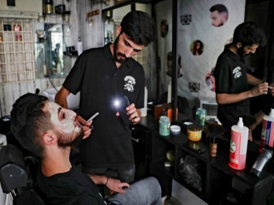 Un coiffeur utilise la lumière de son téléphone portable pour s'éclairer dans son salon, le 20 août 2021 à Beyrouth, au Liban - ANWAR AMRO [AFP]