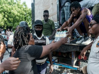 Un homme donne un pack de bouteilles d'eau lors d'une distribution de vivres aux Cayes, ville ravagée par le séisme, le 20 août 2021 - Reginald LOUISSAINT JR [AFP]