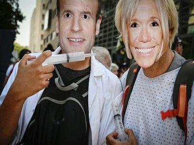 Des manifestants portant des masques d'Emmanuel Macron et de sa femme Brigitte lors d'une manifestation contre le pass sanitaire à Lyon le 14 août 2021 - JEAN-PHILIPPE KSIAZEK [AFP]