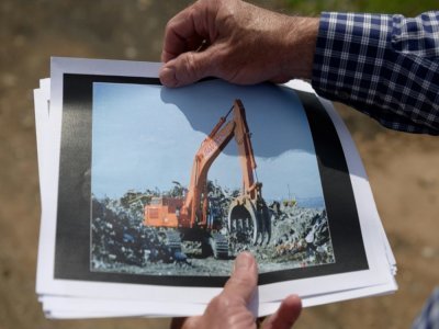 Dennis Diggins montre la photo d'une pelleteuse  en 2001 au milieu des débris du World Trade Center à Fresh Kills, le 28 mai 2021 à Staten Island - Angela Weiss [AFP]