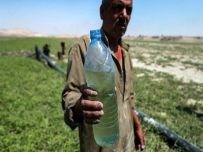 Un homme tient une bouteille d'eau près d'une pompe acheminant de l'eau du lac Assad, le 25 juillet 2021 à Roumeilia, dans le nord de la Syrie - Delil SOULEIMAN [AFP]