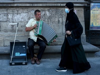 Une touriste des Pays du Golfe passe devant un musicien de rue, le 14 août 2021 à Lviv, en Ukraine - Sergei GAPON [AFP]