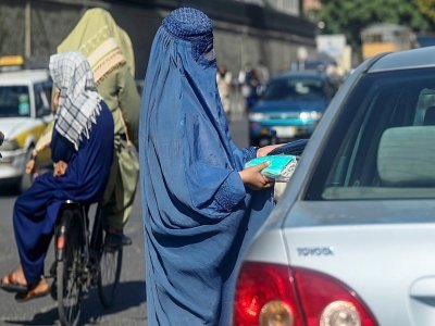Une Afghane en burqa vend des masques de protection à un automobiliste dans une rue de Kaboul, le 5 septembre 2021 - Aamir QURESHI [AFP]