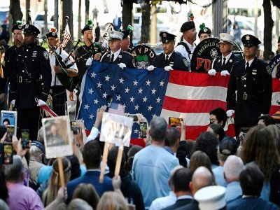 Des policiers et pompiers tiennent le drapeau américain pendant l'hymne national, lors des commémorations pour le 20e anniversaire des attaques du World Trade Center, le 11 septembre 2021 à New York - Jim WATSON [AFP]