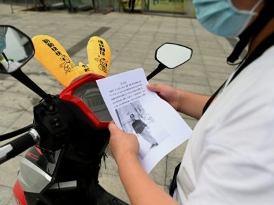 Un livreur examine un avis de recherce pour Chen Shaohua, malade d'Alzheimer disparu, le 19 juillet 2021 à Pékin - NOEL CELIS [AFP]
