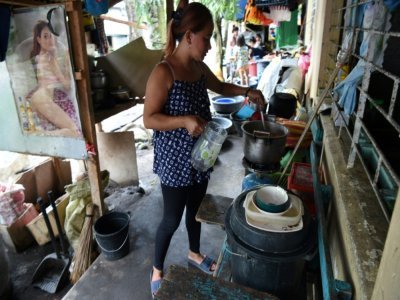 Florivic Baldoza, prépare des repas qu'elle vendra aux ouvriers qui réparent une digue voisine, dans l'école qui sert de logement temporaire à sa famille, dans le village de San Francisco à Guinobatan, aux Philippines, le 5 octobre 2021 - Ted ALJIBE [AFP]
