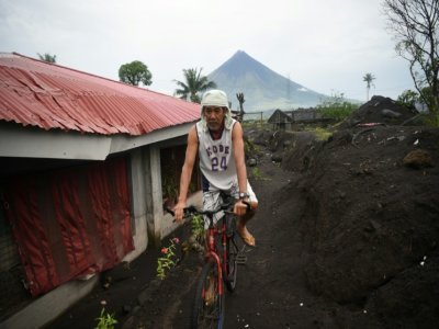 Un homme passe à vélo devant une maison à moitié ensevelie par le sable et les roches suite au typhon Goni en 2020 dans le village de San Francisco à Guinobatan, au sud de Manille, le 5 octobre 2021 - Ted ALJIBE [AFP]