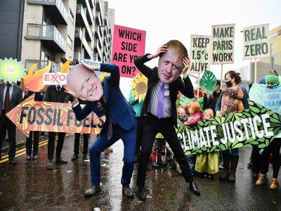 Des militants pour le climat ont revêtu des masques représentant le Premier ministre britannique Boris Johnson (d) et le président américain Joe Biden lors d'une manifestation anti-énergies fossiles à Glasgow, en Ecosse, le 12 novembre 2021 - Ben STANSALL [AFP]