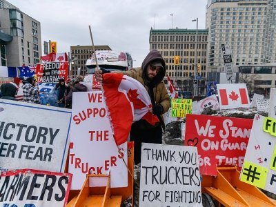 Un manifestant arrange des pancartes et un drapeau canadien, devant le Parlement à Ottawa, le 16 février 2022 - Ed JONES [AFP]