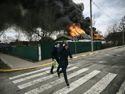 Des personnes courent pour se mettre à l'abri alors que des maisons brûlent après des bombardements, le 4 mars 2022 à Irpin, près de Kiev - Aris Messinis [AFP]