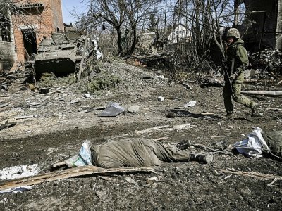 Un homme passe devant le corps d'un soldat russe  gisant au sol, le 28 mars 2022 à Mala Rogan, village à l'est de Kharkiv repris par les troupes ukrainiennes - Aris Messinis [AFP]