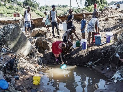 Des hommes sont rassemblés près d'un point d'eau et des femmes remplissent des seaux le 15 avril 2022 près de Durban, après les inondations et glissements de terrain qui ont frappé l'est de l'Afrique du Sud - MARCO LONGARI [AFP]